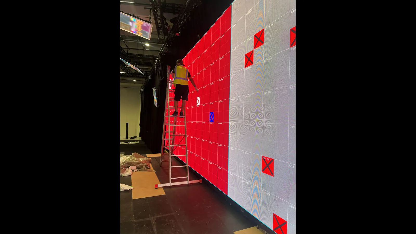 LED technician on a ladder next to precisely marked locations on a large LED wall