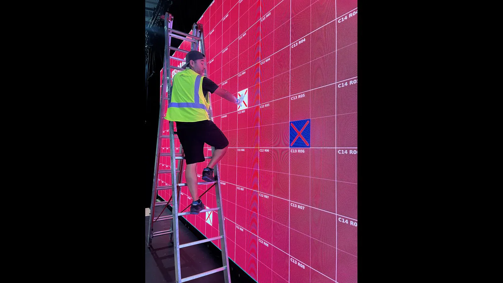 LED technician pointing to a marked module coordinate on a red service grid